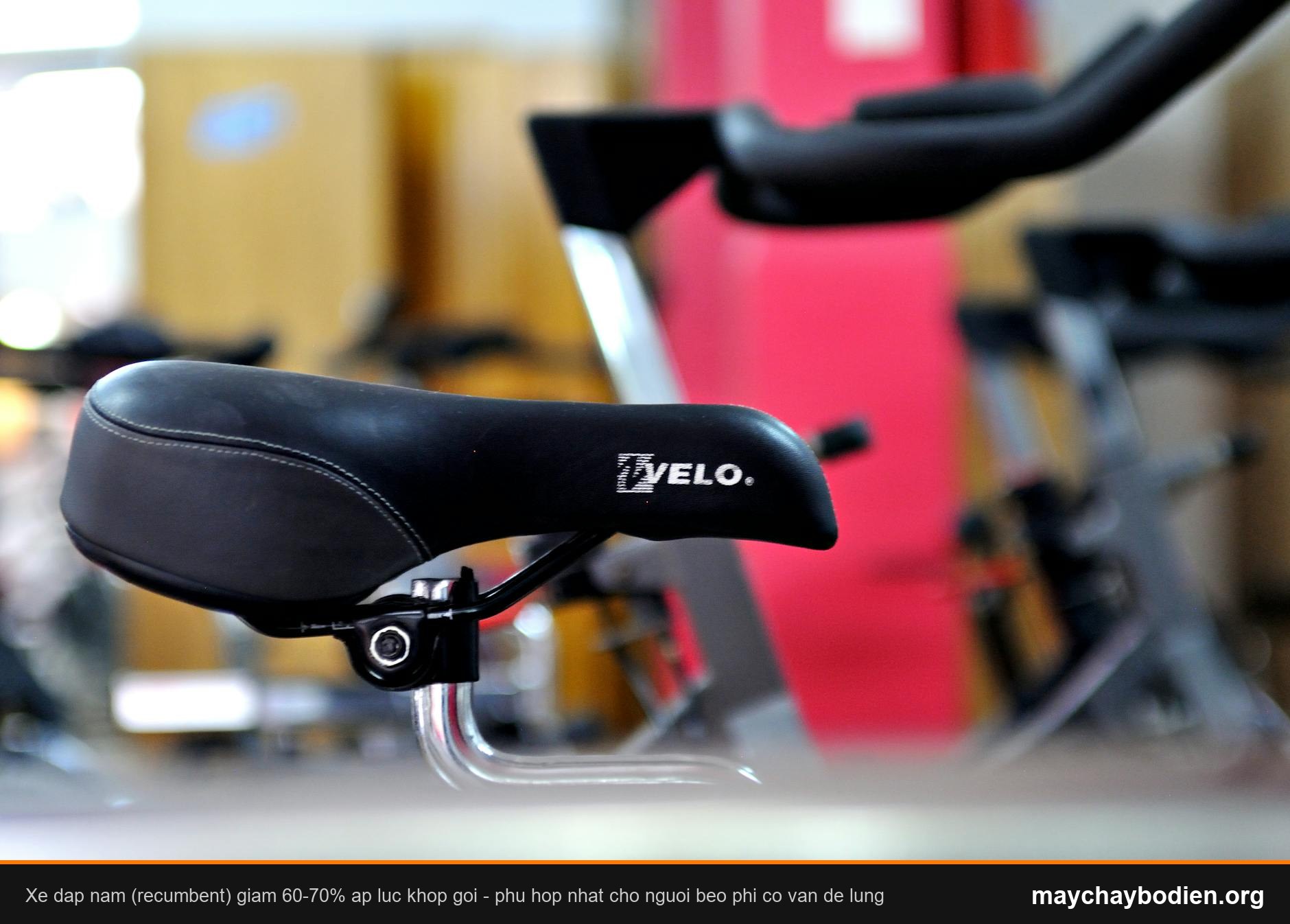 Detailed focus on a black bicycle saddle with gym equipment in the background.